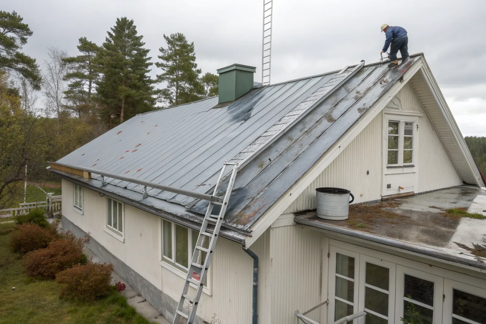 Plåttak som målas om – sliten rostig plåt till vänster, nymålad grafitgrå plåt till höger