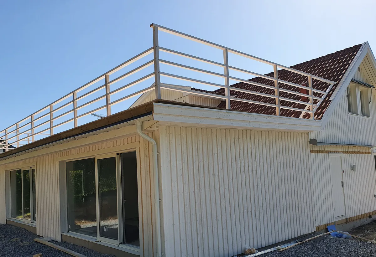 Nybyggd tillbyggnad i ljus träpanel med glaspartier och takterrass med räcke